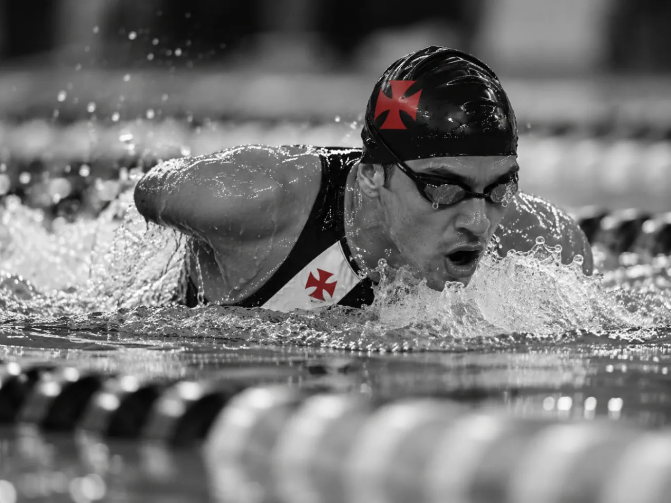 Nadador em movimento na piscina, com touca preta e cruz vascaína